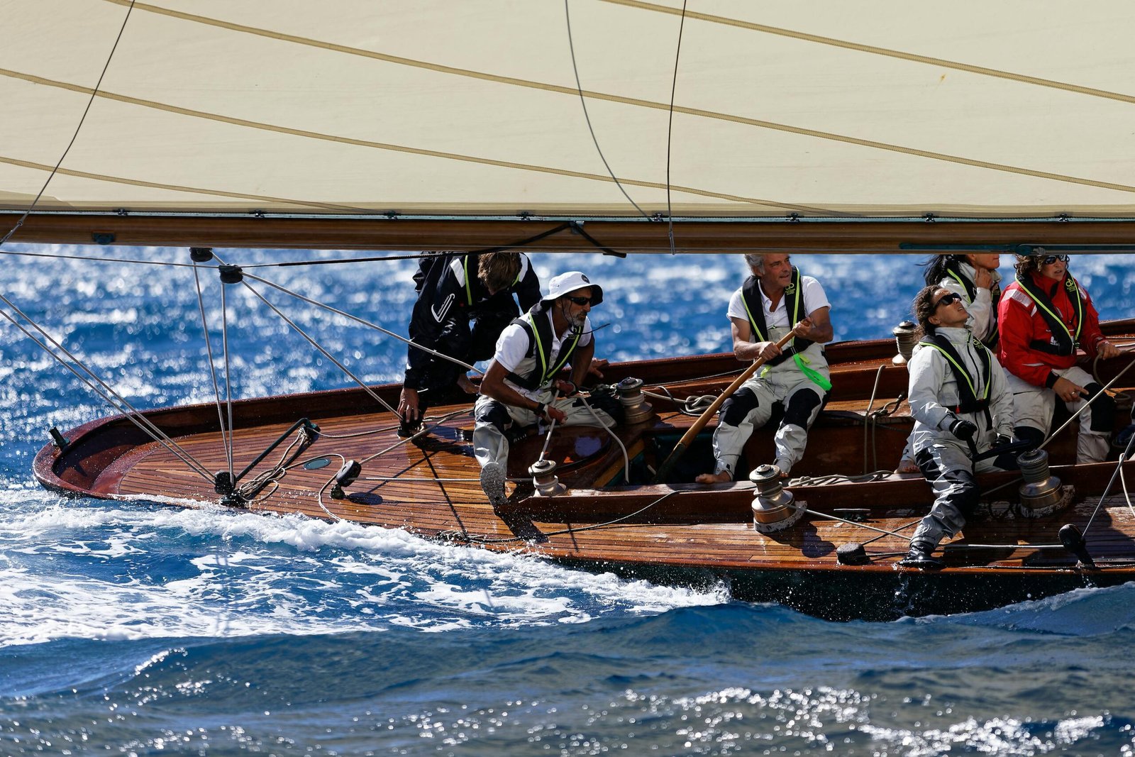 Sailing team maneuvering a classic yacht in vibrant blue waters during a race.